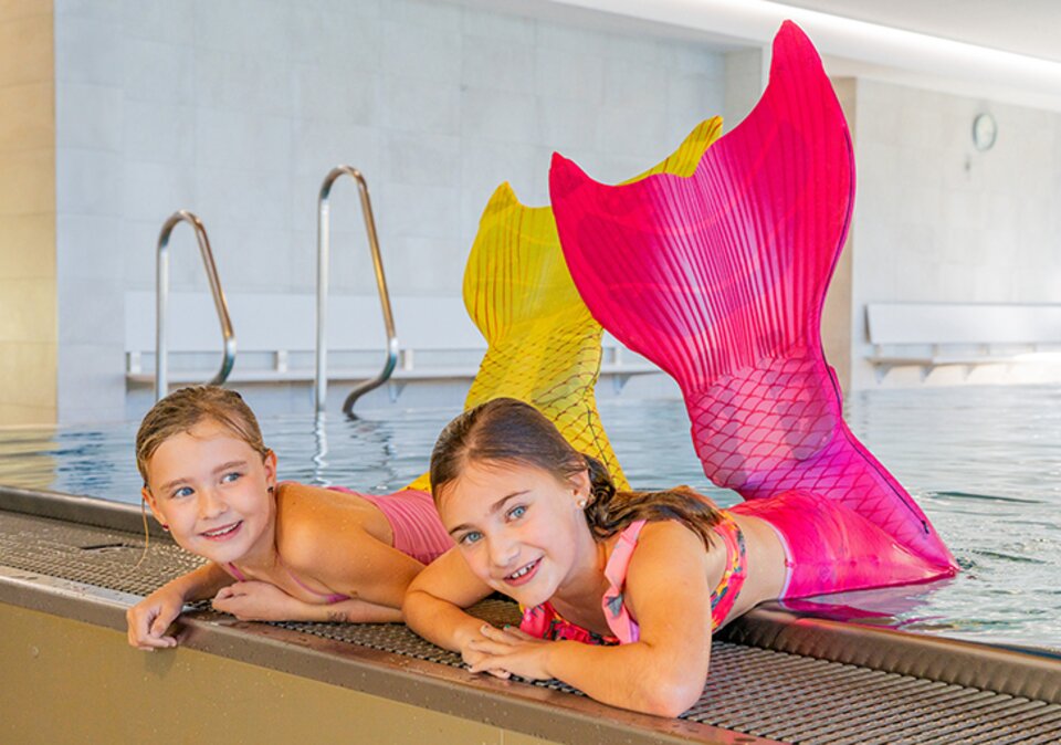 Kinder am Beckenrand im Meerjungfrauenkostüm