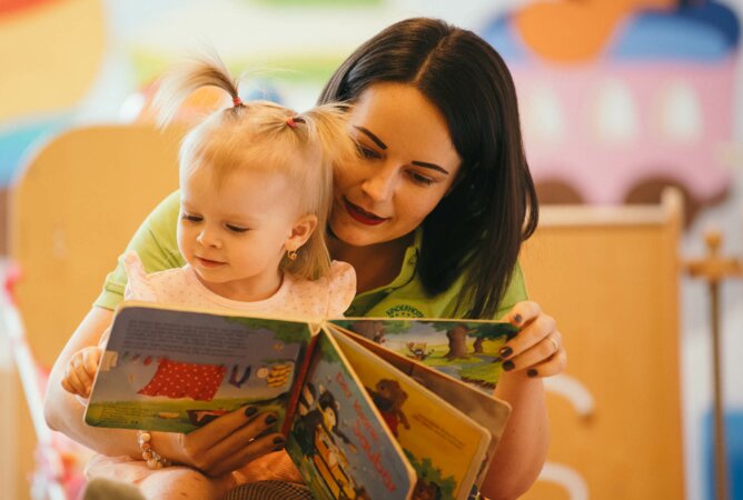 Geschulte Betreuerin liest süßem Kleinkind ein Buch vor