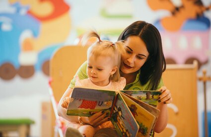Kinderbetreuerin liest kleinem Mädchen ein Buch vor