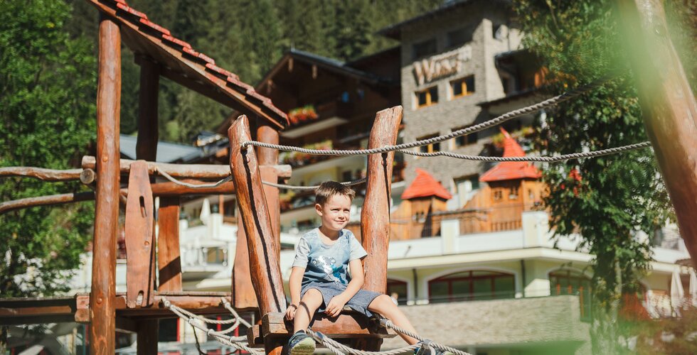 Junge sitzt auf dem Kletterturm auf der Spielealm vor dem Hotel
