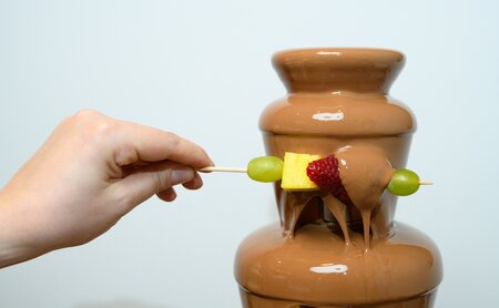 Frische Früchte am Spieß werden unter den Schokoladenbrunnen gehalten