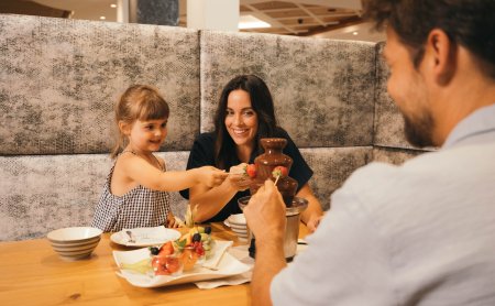 Familie taucht Früchte in Schokobrunnen am Esstisch